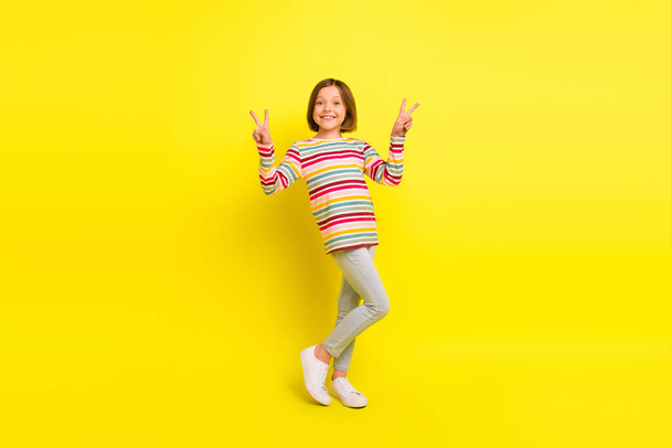 Full body photo of happy nice pretty little girl make fingers v-sings cool mood isolated on bright yellow color background - Foto, Imagem