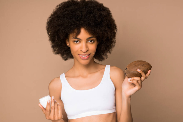 Uma jovem mulata de cabelos encaracolados com um coco e um pote de creme - Foto, Imagem
