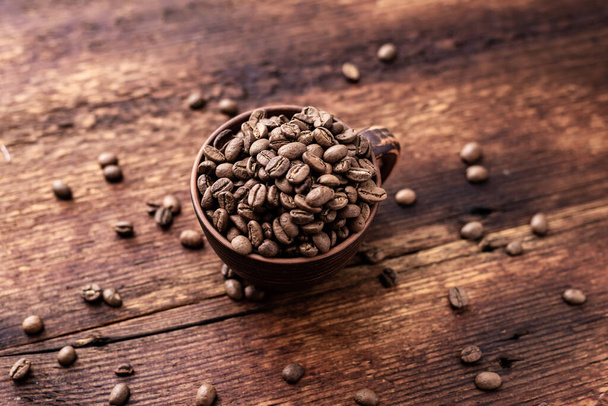 Coffee beans in a clay cup on a brown wooden old background. - Foto, Bild