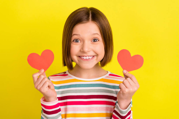 Photo portrait little girl showing two little heart postcards smiling isolated bright yellow color background - Photo, Image