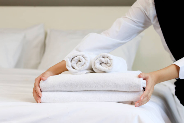 Pokojówka sprzątanie i podejmowania łóżko hotel koncepcja pokoju, kobieta ręce wprowadzenie stosu świeżych białych ręczników kąpielowych na prześcieradle. - Zdjęcie, obraz
