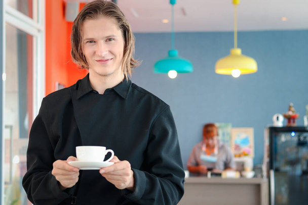 Хансом бариста молодой человек держит чашку горячего кофе в кафе магазин, официанты обслуживают кофе для клиентов в кафе счетчик бар, человек держит напиток в ресторане. - Фото, изображение