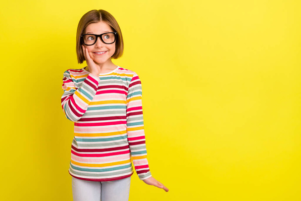 Photo of pretty cute young little girl look empty space hold hand cheek wear glasses isolated on yellow color background - Foto, imagen