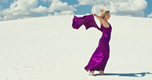 Mozis lassított felvétel egy nőről, aki a homokdűnén sétál. Mezítlábas nő utazó ruhában hintázik a szélben a homokos sivatag hullámzó felszínén, felhővel a háttérben. 4K Szcenírozás - Felvétel, videó