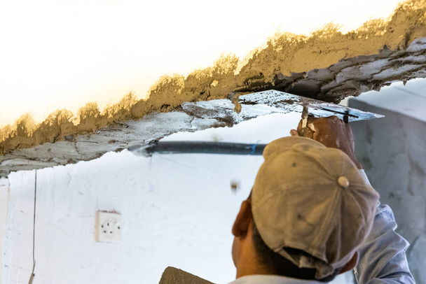 Trabajador enlucido mortero de cemento en viga de techo de hormigón con paleta - Foto, imagen