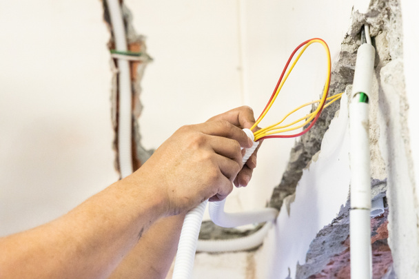Electricista ocultando líneas de cables eléctricos dentro de un tubo de plástico incrustado en la pared - Foto, Imagen