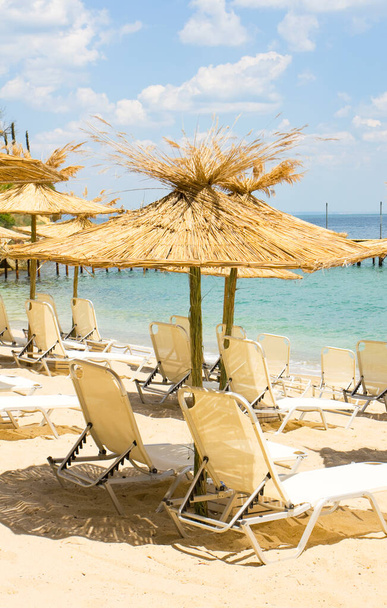 Egzotik saman plaj şemsiyeleri ve deniz kenarındaki kumlu sahilde uzun şezlonglar. Saint Constantine ve Saint Helen tatil beldesinde kaydedildi, Bulgaristan. - Fotoğraf, Görsel