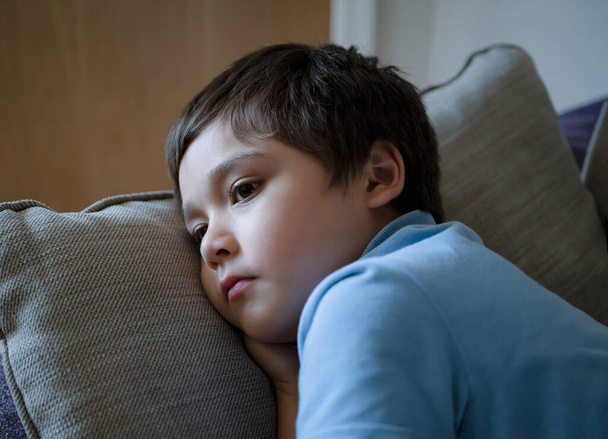 Dramatyczny portret Samotny dzieciak smutna twarz siedzi na kanapie, dziecko siedzi na kanapie w salonie z widokiem głęboko w myślach, chłopiec znudzony pobyt w domu sam. - Zdjęcie, obraz
