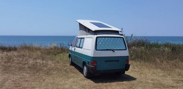 τροχόσπιτο αυτοκίνητο ηλιακά πάνελ ηλεκτρικής ενέργειας από τη θάλασσα το καλοκαίρι παραλία δέντρα μπλε ουρανό ταξίδια στις διακοπές - Φωτογραφία, εικόνα