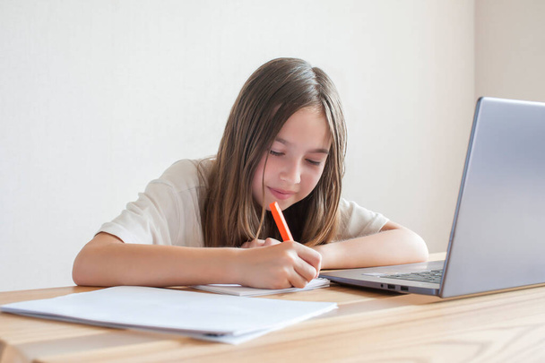 Dziewczynka uczy się przy komputerze w domu przy stole z książkami i notatnikami. Trening online, nauka na odległość, kwarantanna. Pojęcie  - Zdjęcie, obraz