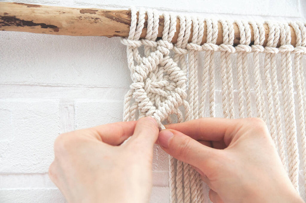 woman knits weaving macrame pinned on a wooden stick near a white brick wall - 写真・画像