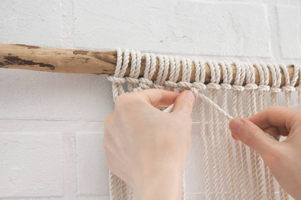 woman knits weaving macrame pinned on a wooden stick near a white brick wall - Photo, image