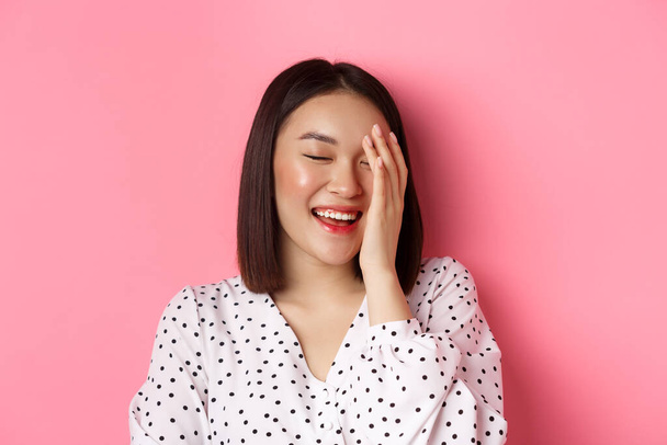 Krása a životní styl. Detailní záběr šťastné asijské ženy smějící se, vypadá šťastně a ukazuje skutečné emoce, stojící nad růžovým pozadím - Fotografie, Obrázek