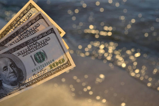 Триста долларов купюр на фоне морской поверхности. 100 долларов наличными - Фото, изображение