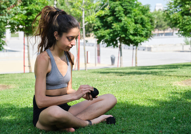 No binary person wearing muay thai hand wraps sitting on grass in a park - Photo, Image