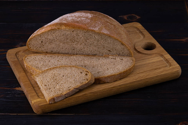 Karanlık bir arka planda kesme tahtasındaki çavdar ekmeği. Dilimlenmiş ekmek. - Fotoğraf, Görsel