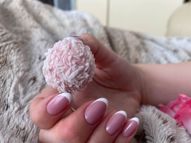 A beautiful female hand with pink nails and manicure is holding a beautiful pink delicious sweet candy. - Photo, Image