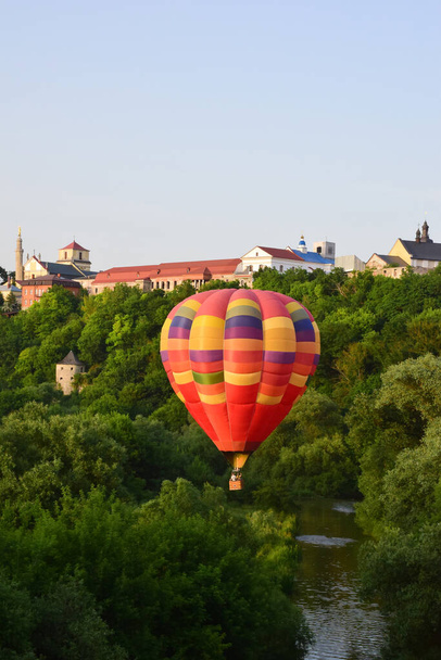 大規模な多色の気球は、川の上と密生した木々の間を非常に低く飛ぶ。背景には、古代都市の建物 - 写真・画像
