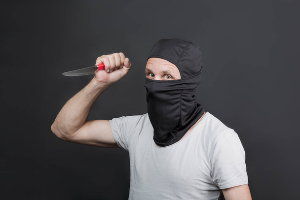 Metal knife in the hand of caucasian man in black mask. The criminal with a knife weapon threatens to kill. With space for an inscription. News staties, newspaper, social issues. american man - Photo, image