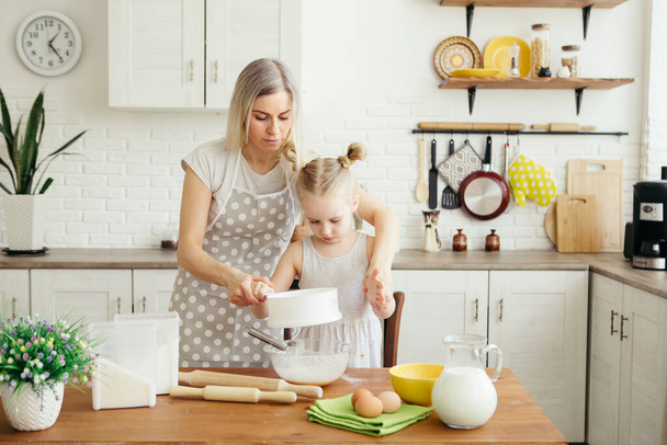 Cute little girl helps mom bake cookies in the kitchen. Happy family. Toning. - Foto, afbeelding