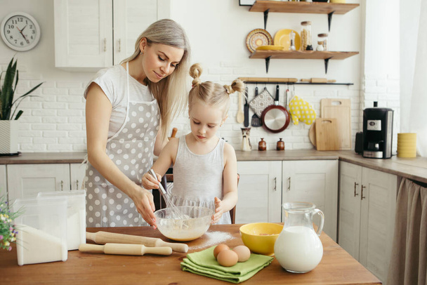 Cute little girl helps mom bake cookies in the kitchen. Happy family. Toning. - Фото, изображение