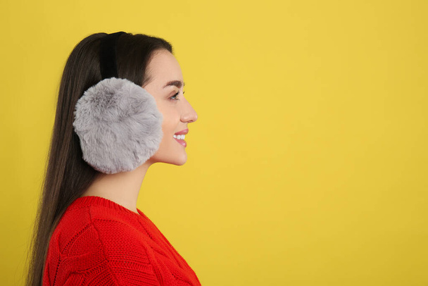 Beautiful young woman wearing earmuffs on yellow background. Space for text - Foto, immagini