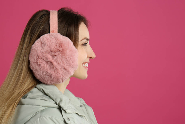 Happy woman wearing warm earmuffs on pink background, space for text - Foto, afbeelding