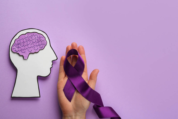 Woman holding purple ribbon near paper human head cutout over violet background, top view. Epilepsy awareness - Foto, afbeelding