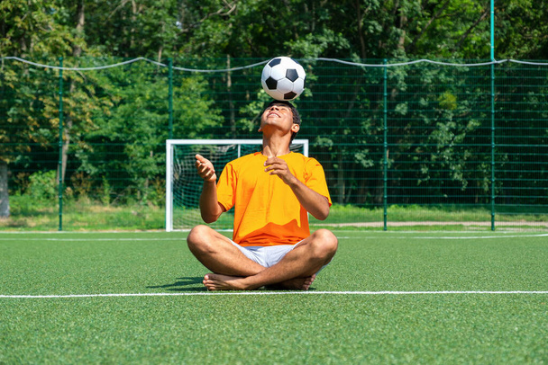 Brazilian soccer player trains and improves soccer ball control by juggling it on his head sitting on sport ground in summer - Foto, imagen
