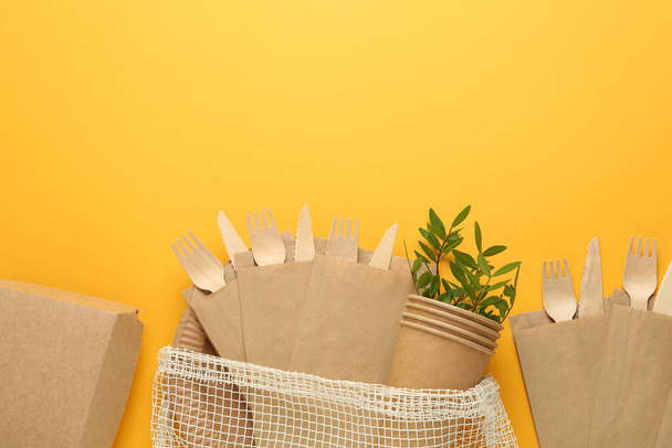 Flat lay of paper and wooden tableware with green twigs on yellow background, space for text. Eco friendly lifestyle - Foto, imagen