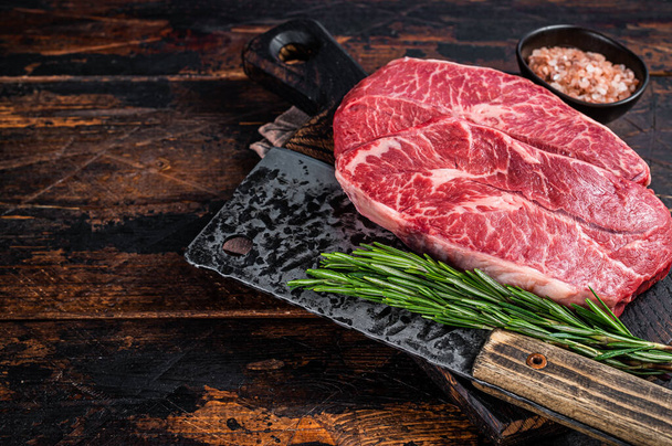 Tepelně neupravené hovězí steaky v horní části ramene nebo ploché železo na dřevěné řezbářské desce se sekáčkem na maso. Tmavé dřevěné pozadí. Top View. Kopírovat prostor - Fotografie, Obrázek
