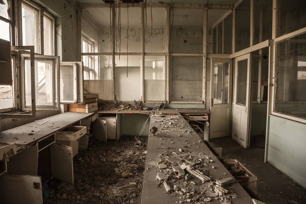Interno di un edificio per uffici abbandonato, in una stanza sporca e danneggiata, con una vecchia scrivania rimasta dopo la chiusura e il fallimento dell'attività. - Foto, immagini
