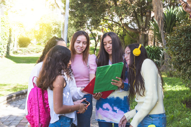 Grupa latynoskich nastolatek z plecakami i notatnikami przegląda pracę domową w drodze do liceum - Zdjęcie, obraz