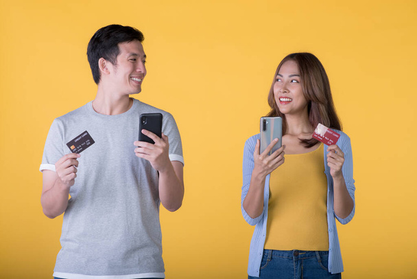 Izgatott ázsiai pár kezében hitelkártya és okostelefon érzés izgatott elszigetelt színes háttér - Fotó, kép