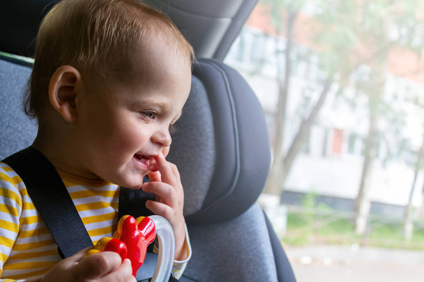 Unrecognizable caucasian baby sitting in car seat, holding toy in hands, playing and smiling. Toys for trips in car with kids. Summer vacation.  - Foto, immagini