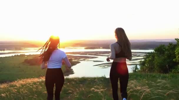 Two young women in sports clothes jogs around the field at early sunset - Footage, Video