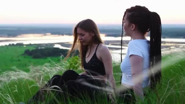 Két fiatal nő ül a fűben, beszélgetnek, aztán felállnak és elfutnak. - Felvétel, videó