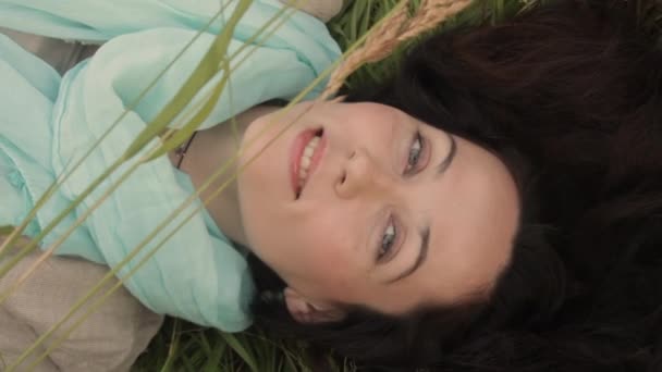 Νεαρή γυναίκα χαλαρώνει ξαπλωμένη στο γρασίδι του αγρού. - Πλάνα, βίντεο