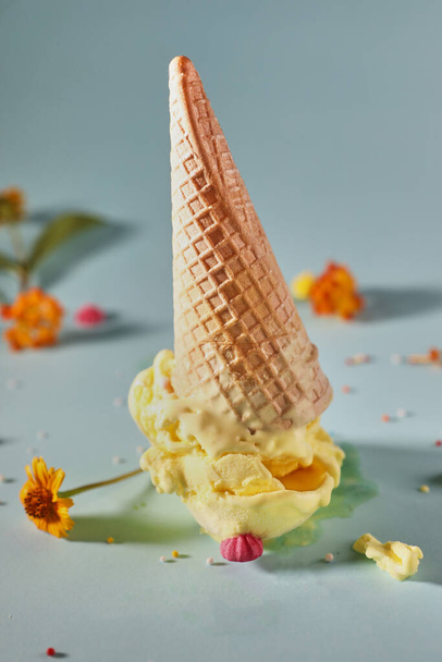 Crème glacée à la mangue avec cône de gaufre sur fond bleu avec fleurs jaunes. - Photo, image