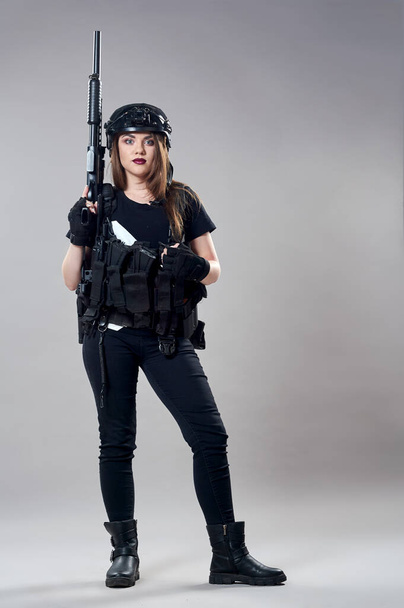 Молода жінка з кулеметом у руках на сірому фоні
 - Фото, зображення