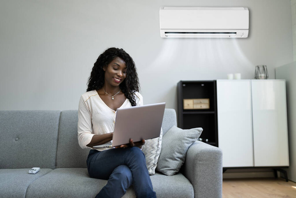 Young Happy Woman Sitting On Couch Using Air Conditioner At Home - Photo, Image