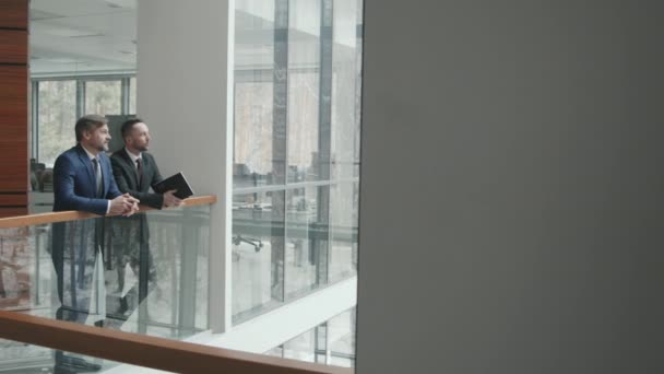Медленное движение Широкий PAN снимок двух успешных бизнесменов или адвокатов, говорящих, опираясь на перила в современном офисе - Кадры, видео