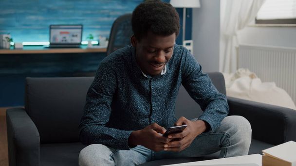 Fekete fickó a nappalijában telefonnal böngészi a közösségi médiát - Fotó, kép