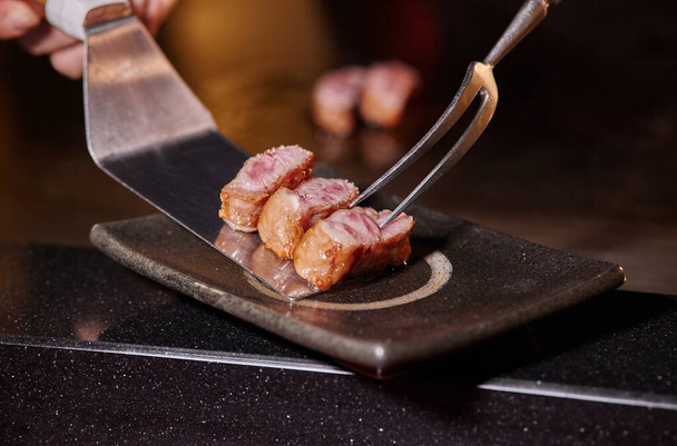 Japonský kuchař vaří ručně krájené lahodné hovězí Kobe nebo Wagyu steak v Teppanyaki stylu. Horké a lahodné pečené hovězí maso, fesa, ranichi - Fotografie, Obrázek