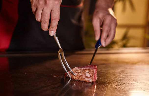 Japanischer Koch kocht von Hand ein in Scheiben geschnittenes köstliches Kobe Beef oder Wagyu-Steak im Teppanyaki-Stil. Heißes und köstliches Roastbeef, Fesa, Ranichi - Foto, Bild