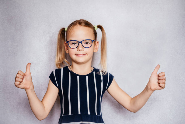 Menina vestindo óculos com os polegares para cima, crianças Oftalmologia Pediátrica, problemas oculares comuns em crianças - Foto, Imagem