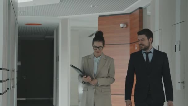 Mediana lentitud de pareja de jóvenes abogados exitosos en ropa formal hablando de trabajo mientras camina a través de la oficina moderna - Imágenes, Vídeo
