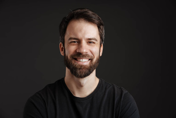 Bearded brunette man smiling and looking at camera isolated over black background - Fotografie, Obrázek