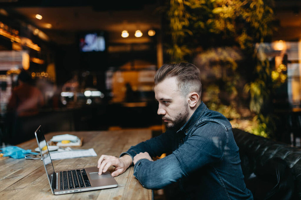 Male freelancer sits in a cozy coworking cafe and works online with a laptop, online business - Zdjęcie, obraz