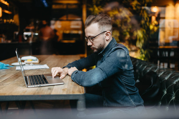 Male freelancer sits in a cozy coworking cafe and works online with a laptop, online business - Foto, Bild